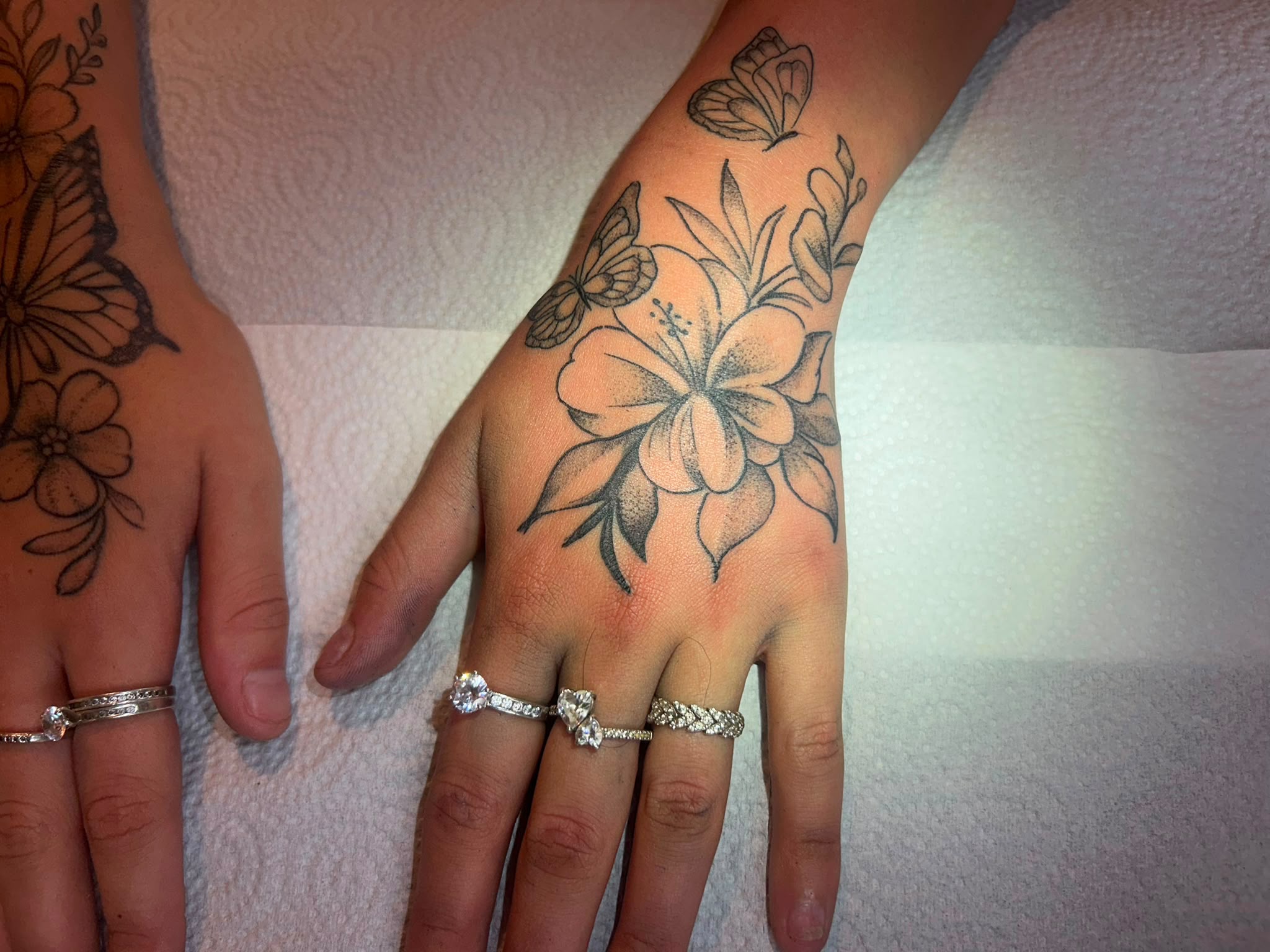 Fine line floral and butterfly hand tattoo